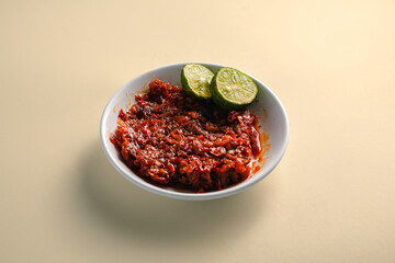 Indonesian spicy sambal with a half-cut lime, served on a white plate, isolated on a white background