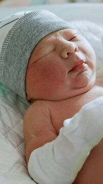 Sweet new born baby in a cap and mittens. Nurse's gloved hands changing a diaper to a Caucasian infant. Close up. Vertical video