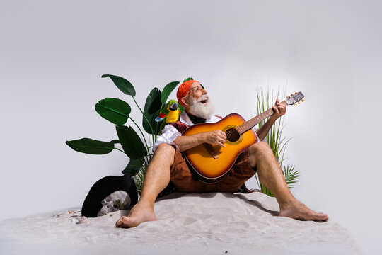 Joyful elderly pirate playing guitar on sandy beach with lush greenery and parrot, showcasing a whimsical blend of music and adventure