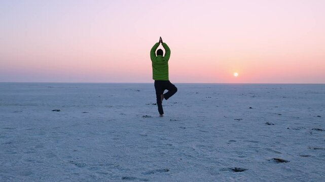 young man performing yoga in white desert with sunrise orange dramatic sky at dawn