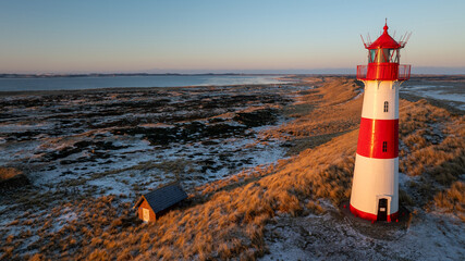 Red and white striped lighthouse situated on a coastal landscape at sunrise in winter. Lighthouse...