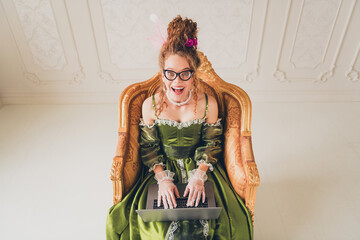 Elegant woman in historical dress using a laptop, juxtaposing modern technology with a classical...