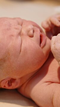 Newborn red-haired baby cries while doctor's gloved hand puts stethoscope to its chest. Checking the life of a child after birth. Close up. Vertical video