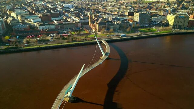 Wide advancing aerial shot of the Peace Bridge and Guildhall in Derry-Londonderry. Filmed on a sunny day in 4K, 60 frames per second and in Rec709 color.