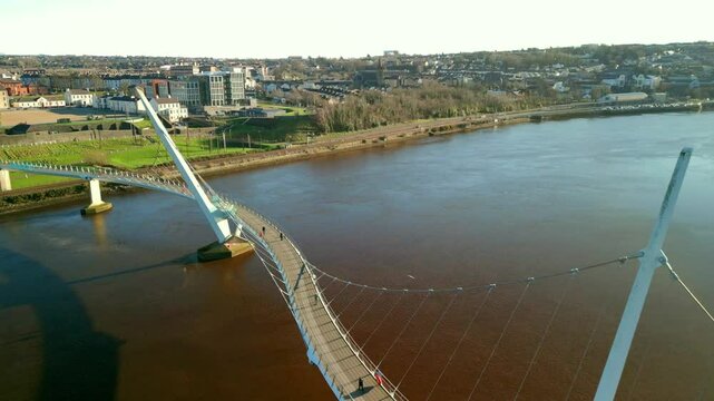 High, passing aerial Rising aerial shot of the Peace Bridge in Derry-Londonderry. The camera passes over the bridge. Filmed on a sunny day in 4K, 60 frames per second and in Rec709 color.