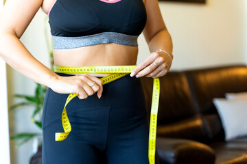 Woman measuring her waist with a yellow tape measure after dieting