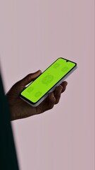 Black African-American young male using smartphone with a blank green screen. Mobile app video mockup. Vertical phone orientation