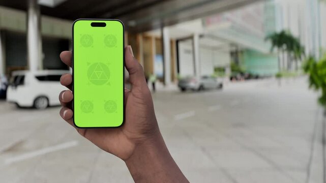 GREEN SCREEN CHROMA KEY Smartphone with a green screen held in a hand near a hotel entrance, featuring a parked car and modern urban surroundings