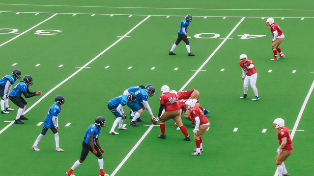 Two American Football Teams Stand Across From Each Other on the Line of Scrimmage as the Ball is Ready to be Passed to Start the Game. Gridiron Players Ready to Tackle and Defend