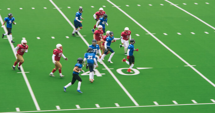 American Football Players in Blue Jerseys Sprinting to Make a Goal. Authentic Gridiron Game on a Big Green Outdoors Field with Markings. Opposing Teams Playing a Tournament Match