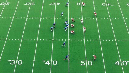 Aerial High Angle Shot of Red and Blue American Football Teams Strategically Lining Up and Facing the Opponents. Intense Match Start with Athletic Players Fight for the Ball and Defend Positions