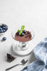 Chocolate pudding in a glass with fresh blueberries and mint on a light background