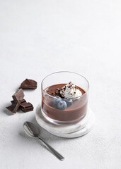 Chocolate pudding in a glass with whipped cream and fresh blueberry on a light background