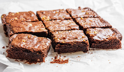 Chocolate brownie with nuts cut into pieces on baking paper close-up with morning light.