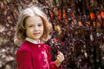 Spring blooming. Portrait of a beautiful 5-year-old girl in a red dress in a blooming garden in nature. Childhood.