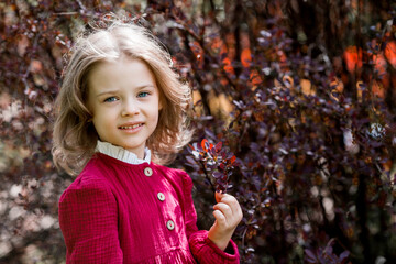 Spring blooming. Portrait of a beautiful 5-year-old girl in a red dress in a blooming garden in nature. Childhood.