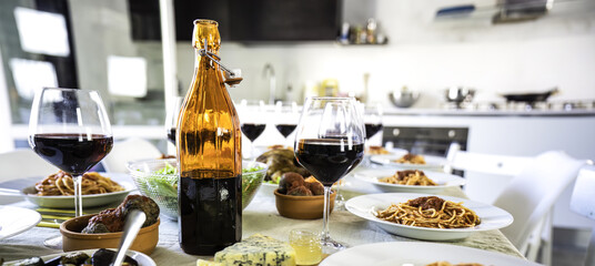 Italian dining table with wine and pasta dishes. Close-up of a rustic glass bottle and glasses of red wine surrounded by traditional Italian cuisine.