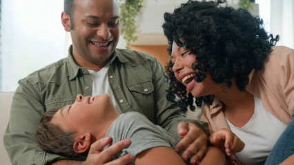 Happy multiracial family parents playing with cute little boy son tickling have fun laugh together...
