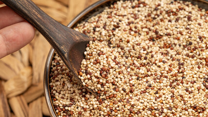 Hand holding a wooden spoon filled with mixed quinoa grains above a bowl. Rustic and healthy food...