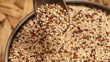 Rustic wooden spoon scooping mixed quinoa grains from a bowl. Healthy food concept with organic superfood grains.