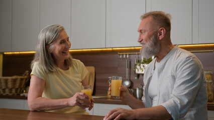 Caucasian married couple happy retired family elder man husband talking with mature woman wife in kitchen laughing male female drinking orange juice fresh fruits healthy nutrition love relationship