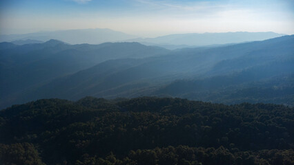 Beautiful sunrise on the mountain in winter. The sun shines down on a serene mountain landscape covered with tropical trees in the early morning.