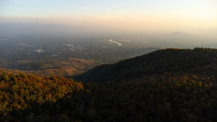 Fototapeta premium Beautiful sunset in the winter mountains. The setting sun shines down on a serene mountain landscape covered with tropical trees in the evening.