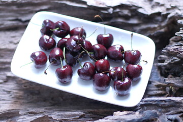 Red cherries with stems in a white plate on a wooden background