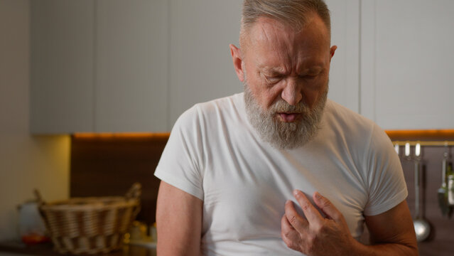 Ill sick Caucasian grandpa old senior male feeling bad at kitchen unhealthy unwell elderly man pain in chest heart attack heartburn heartache mature woman wife help husband call emergency with phone - Powered by Adobe