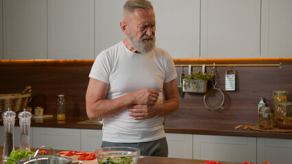 Ill sick Caucasian grandpa old senior male feeling bad at kitchen unhealthy unwell elderly man pain in chest heart attack heartburn heartache mature woman wife help husband call emergency with phone