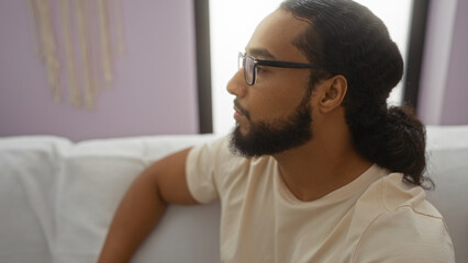 Fototapeta premium Young man with beard relaxing indoors in a comfortable living room setting with natural light.