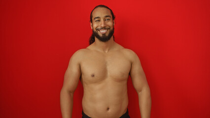 Fototapeta premium Young man with beard smiling confidently against an isolated red background showcasing strength and vitality