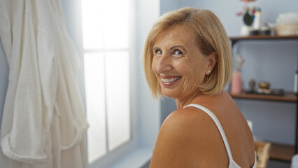 Fototapeta premium Mature woman with short blonde hair smiling indoors at a spa or beauty center with soft lighting and serene atmosphere
