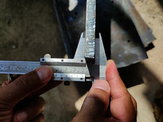Close-up of hands using a caliper to measure a metal beam for precise engineering work