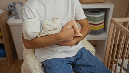 Young man in hospital room holding baby in arms near cradle wearing casual clothes showing care and tenderness in warm indoor setting highlighting paternal love and serenity