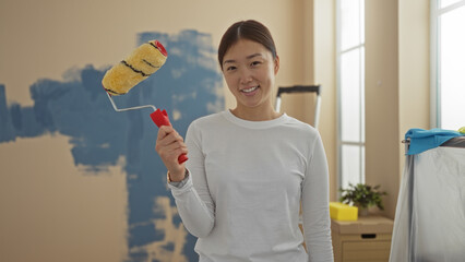 Woman smiling while holding paint roller indoors, showcasing her diy spirit in a bright living room...