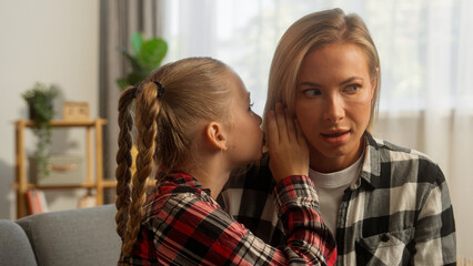 Shocked Caucasian female mother woman listening family kid daughter whisper gossip at home smiling...