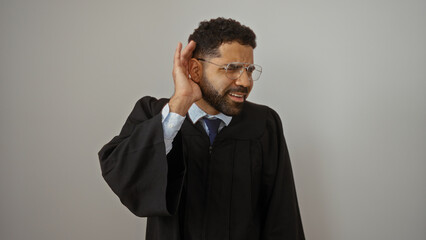 Obraz premium Handsome young man in graduation gown posing isolated against white background maintaining an attentive hand to ear gesture