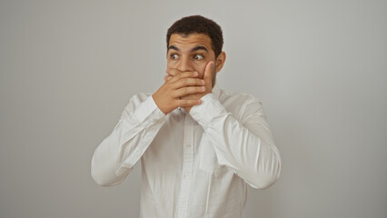 Fototapeta premium Young hispanic man covering mouth with hands in shock isolated on white background