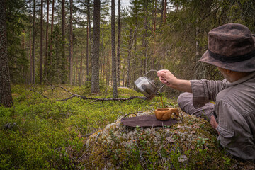 Man pouring coffee from a kettle into a wooden cup while resting in the forest