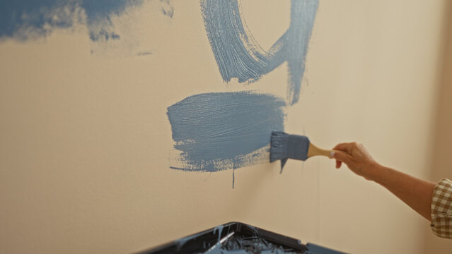 Woman painting wall with blue paint brush indoors, showcasing diy home renovation in new apartment with natural light. - Powered by Adobe