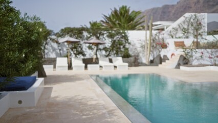 Defocused tropical resort poolside with blurred lounge chairs, umbrellas, and lush greenery,...