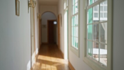 Blurred indoor hallway with sunlight streaming through windows leading to a doorway capturing a peaceful atmosphere with defocused wall decorations in a cozy setting