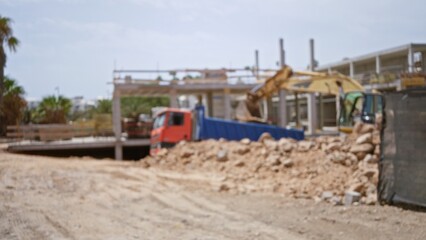 Blurred construction site with defocused excavator and truck in foreground showcasing building...