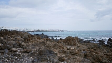 Blurred coastal scene on lanzarote in the canary islands, spain with rocky shores and distant buildings in an outdoor setting.