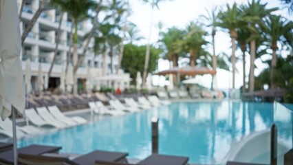 Blurred tropical resort pool area with palm trees and lounge chairs in the background, creating a vacation bokeh effect
