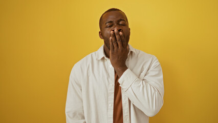 Handsome young man yawning over isolated yellow background wall in a tired expressive gesture.