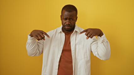 Young man with sad expression poses against a vibrant yellow background, conveying a thoughtful...