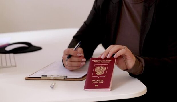 Close up of a woman filling out visa application documents with a Russian passport on a office table