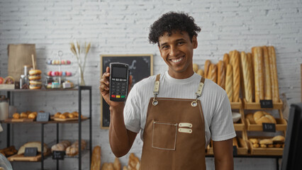 Young hispanic man smiling in bakery holding payment terminal indoors